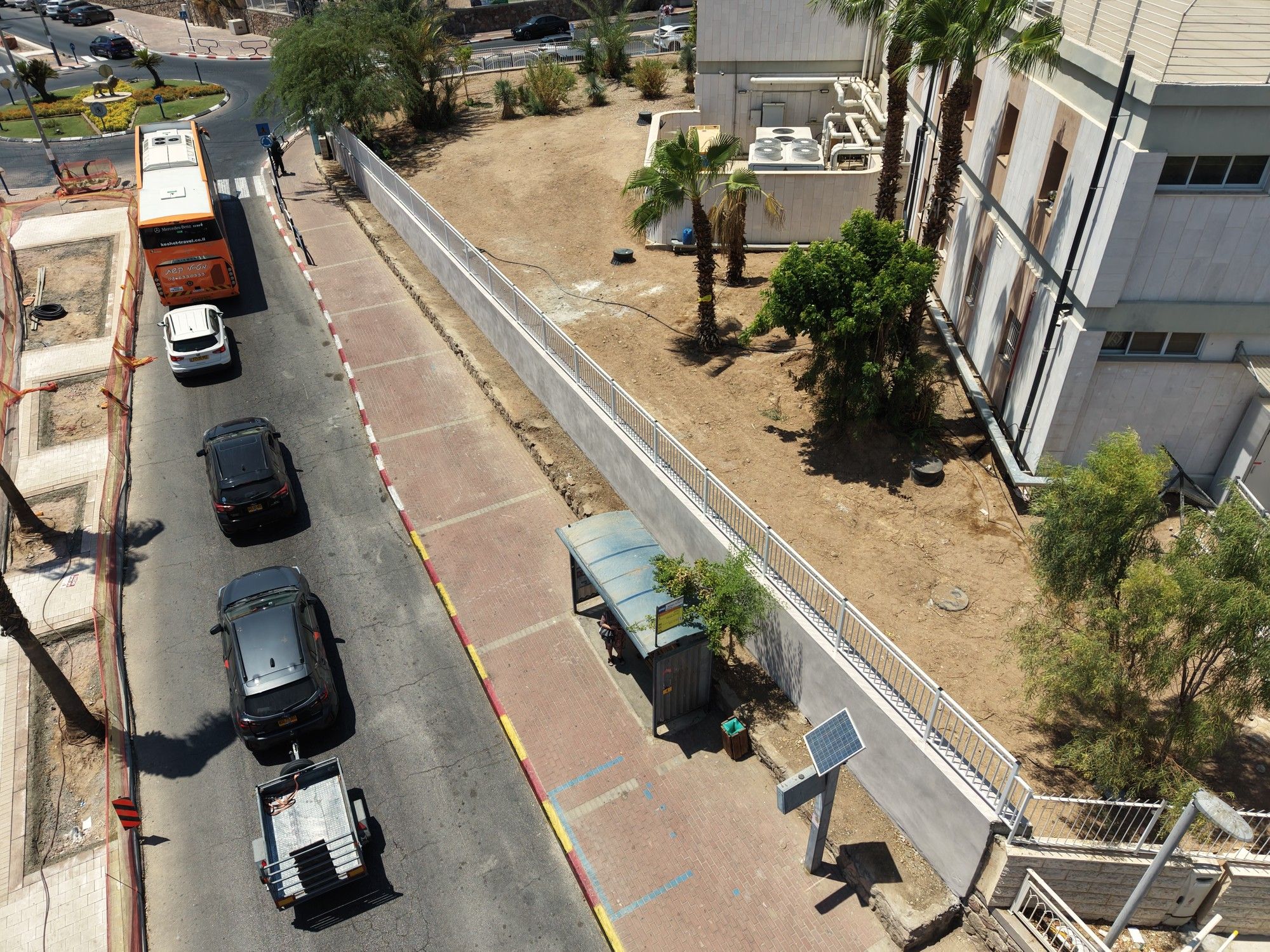 מדרכה אדומה ומעקה לבן לאורך הרחוב, ותחנת אוטובוס