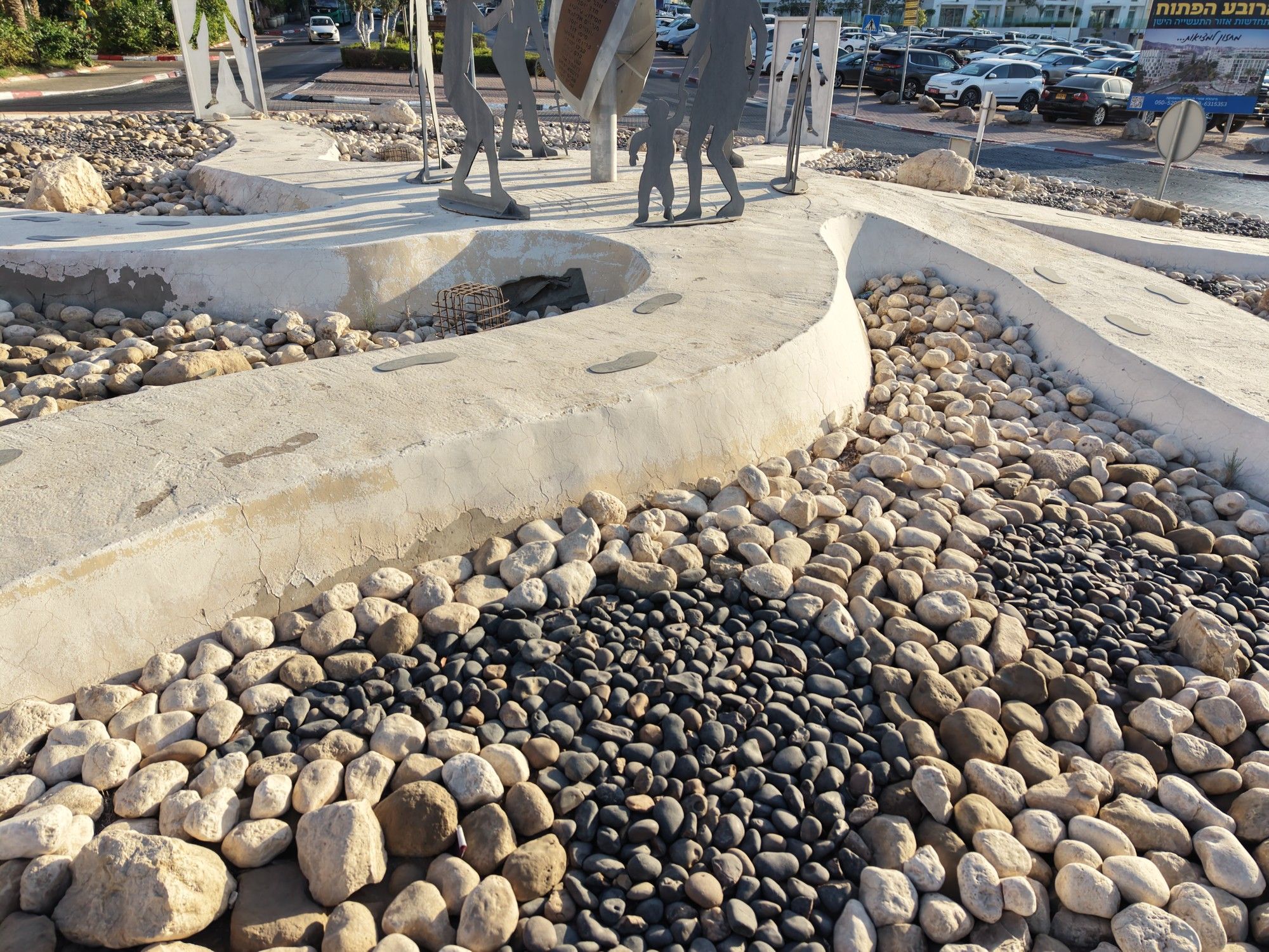 חלוקי נחל בהירים וכהים לצד שביל לבן — פרט מהכיכר