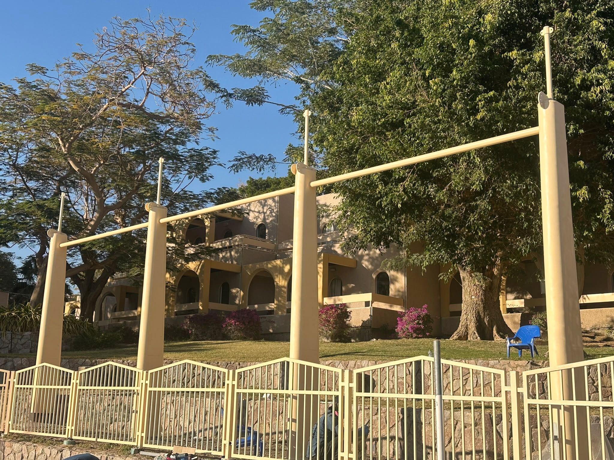 עמודים וקורות של פרגולה וגדר נמוכה, בגן מול מבנה ותיק