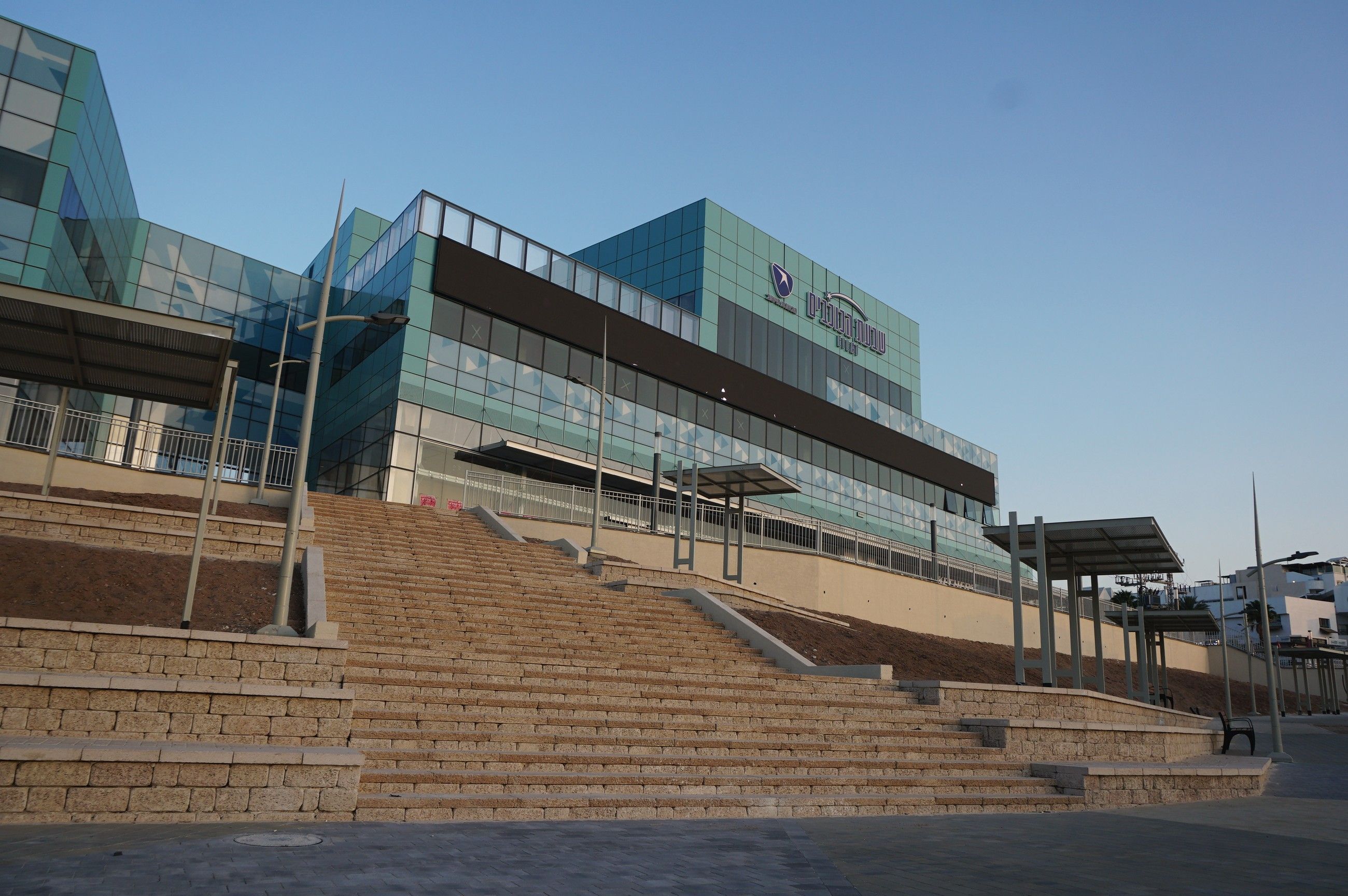 מדרגות אבן רחבות ורחבה מרוצפת מול מבנה זכוכית, בפיתוח מתחם קניון שבעת הכוכבים באילת