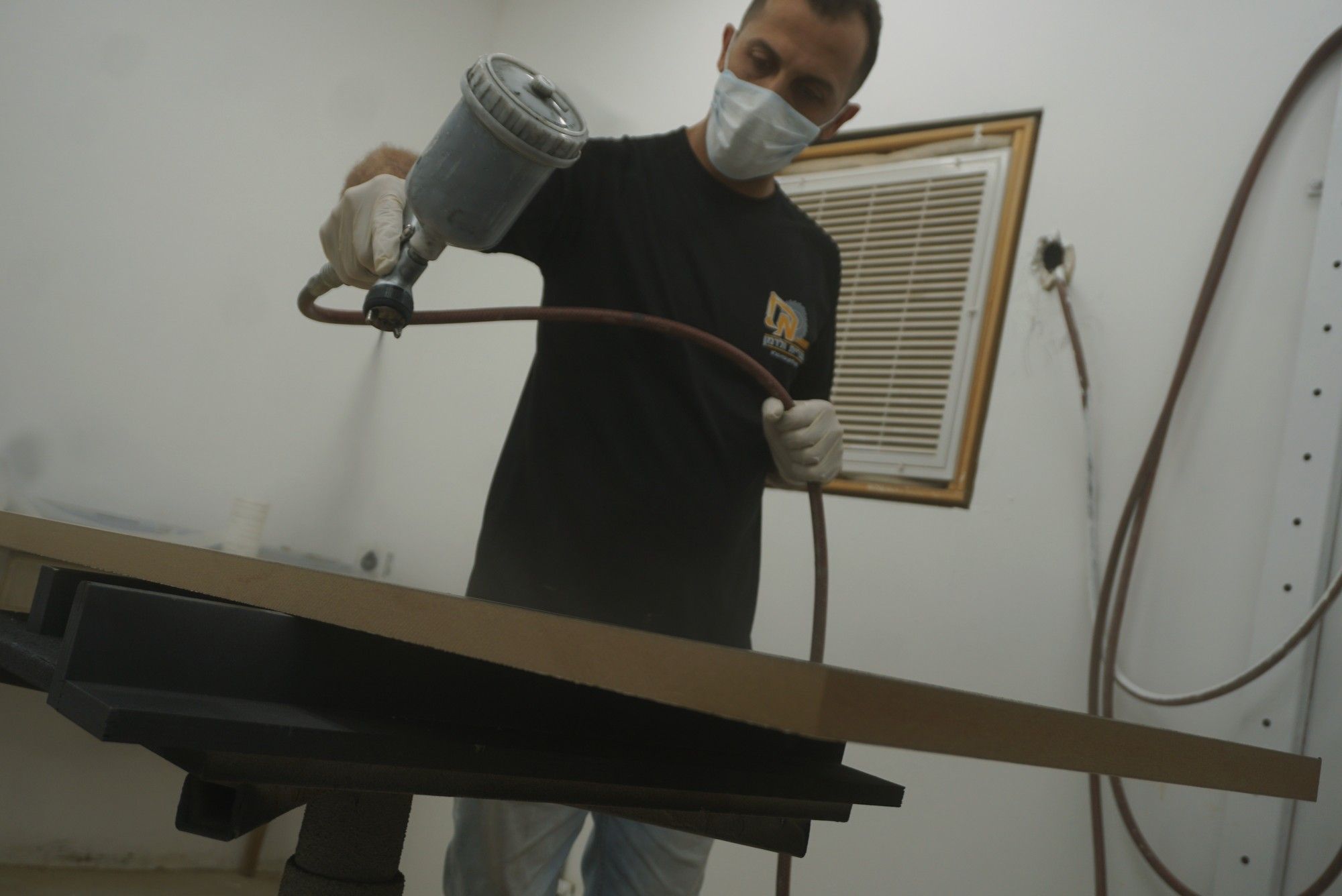 נגר מרסס לכה על משטח עץ כהה בתא הצבע