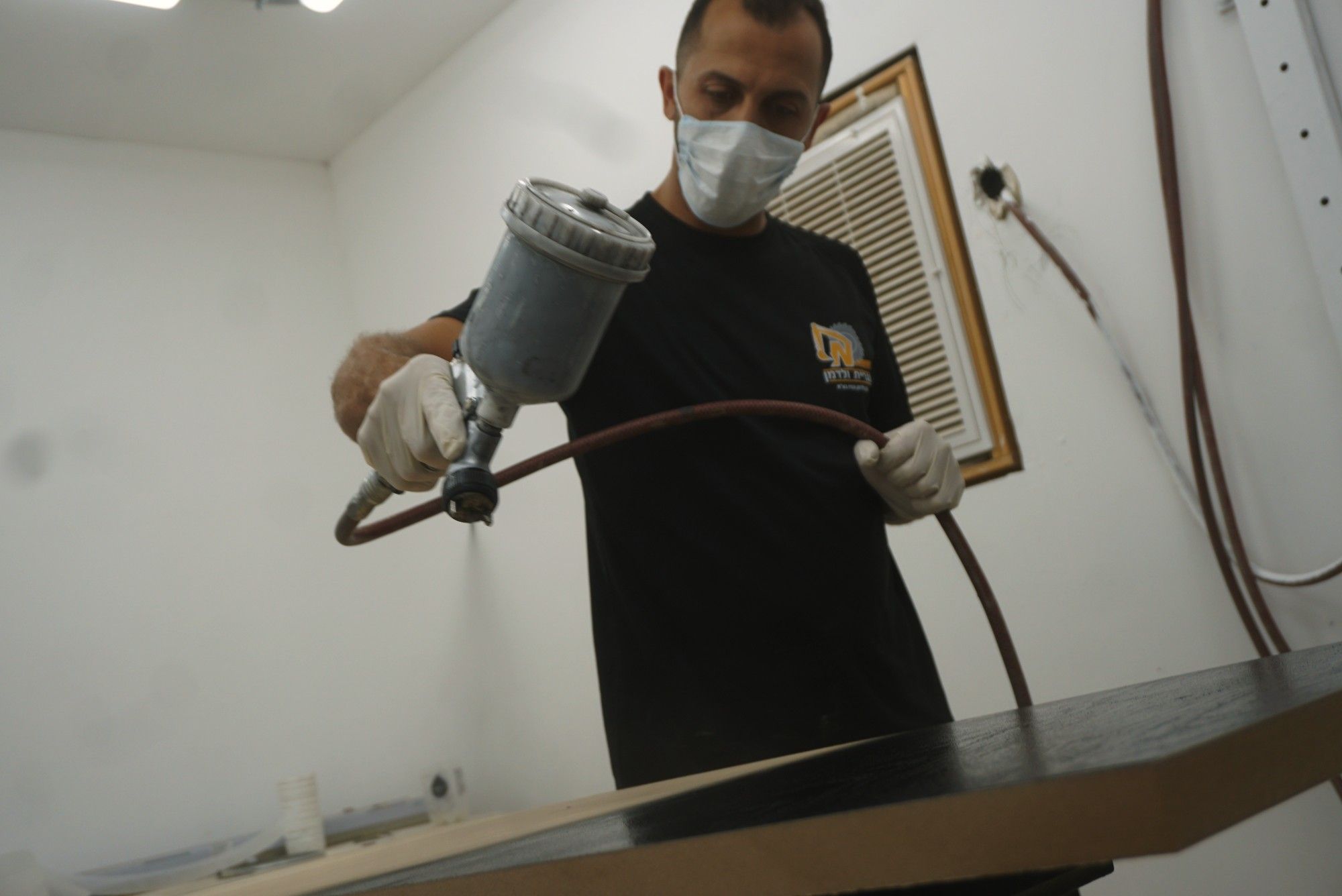 נגר מרסס לכה על משטח עץ בתא הצבע