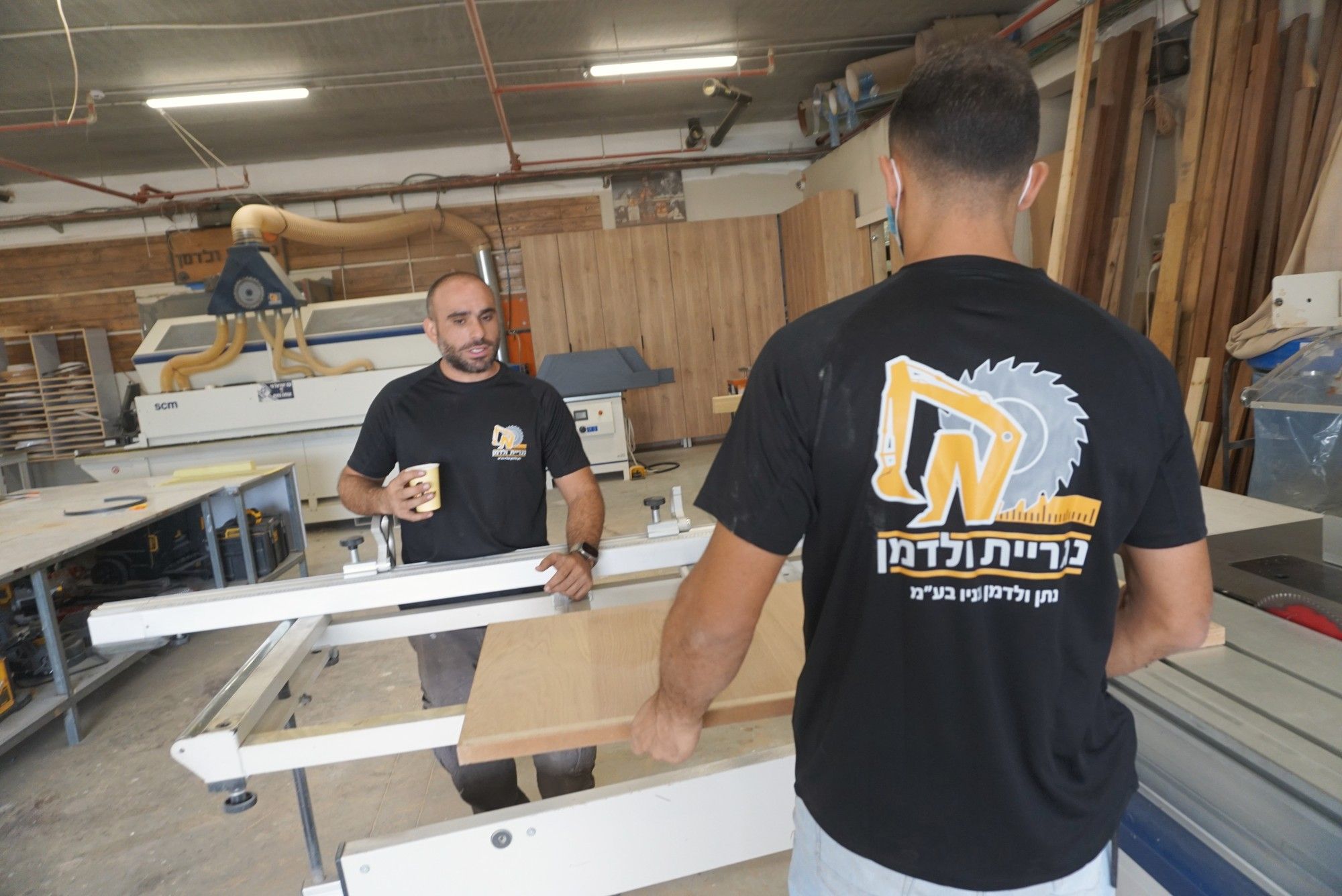 שני נגרים בחולצות נגריית ולדמן עובדים יחד ליד מסור הפאנלים